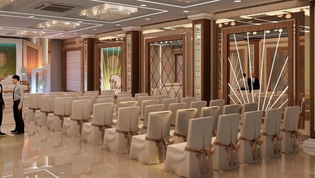 A spacious conference room with rows of chairs, a stage, and decorative wall panels. - Hotel Olive Crown (Lucknow)