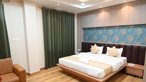 A modern hotel room with a large bed, wooden floor, green curtains, and a patterned headboard. - Hotel Olive Crown (Lucknow)