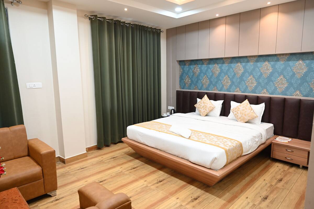 Ein modernes Hotelzimmer mit einem großen Bett, Holzboden, grünen Vorhängen und einem gemusterten Kopfteil.