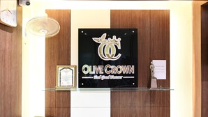 A reception desk with a framed certificate, a plaque, and a sign reading "Olive Crown" with a crown logo. - Hotel Olive Crown (Lucknow)