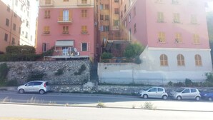 Un immeuble à plusieurs étages doté de balcons, d’un mur en pierre et de voitures garées le long de la rue.