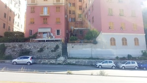 A multi-story building with balconies, a stone wall, and parked cars along the street. - Martino Codice Citra 010 025-lt0801 (Genoa)