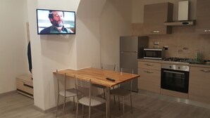 Une cuisine moderne avec un coin repas, comprenant un téléviseur fixé au mur, des appareils en acier inoxydable et une table à manger en bois.