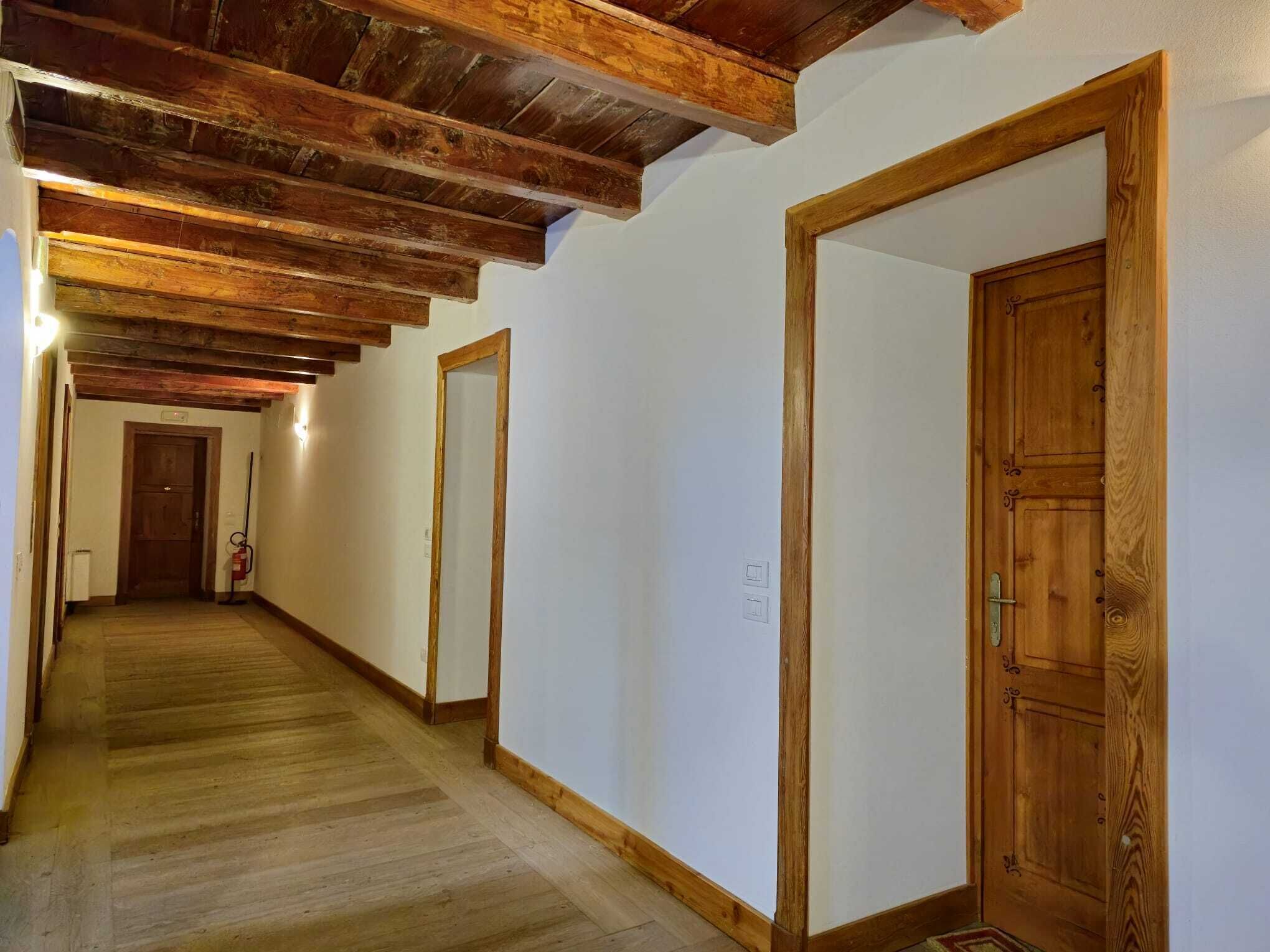 A hallway with wooden beams on the ceiling, wooden doors, and a fire extinguisher.