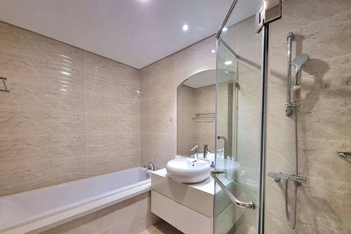 A modern bathroom with a glass-enclosed shower, a white bathtub, and a vanity with a sink.