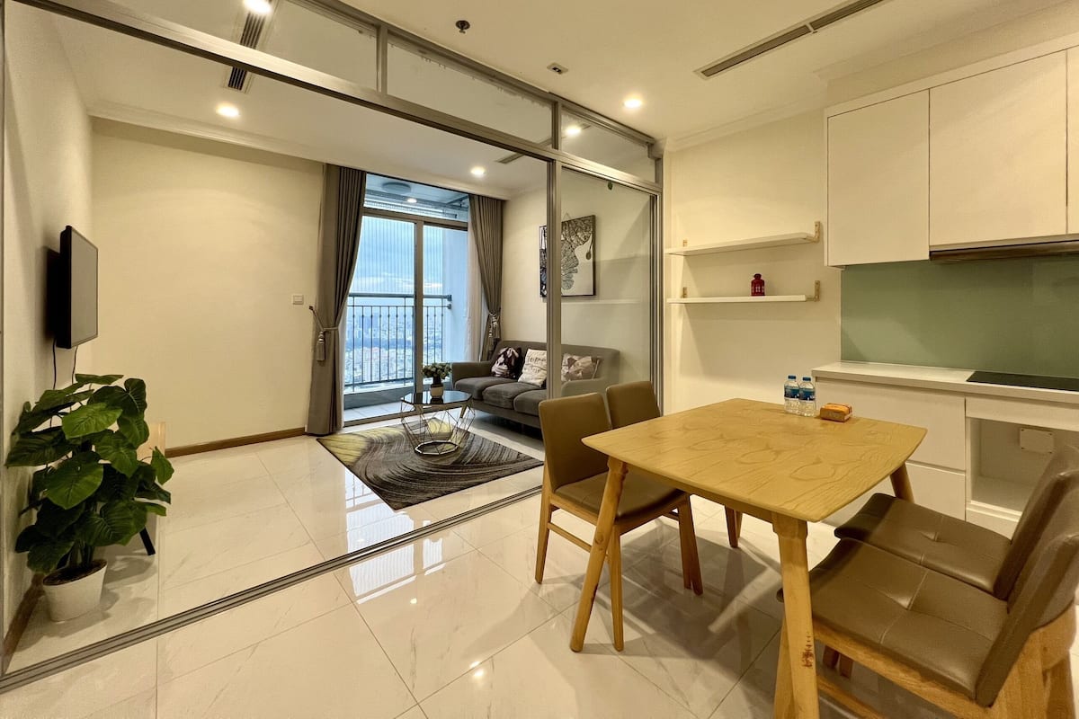 A modern living room with a sofa, a coffee table, and a TV. There is a balcony with a view of the city.