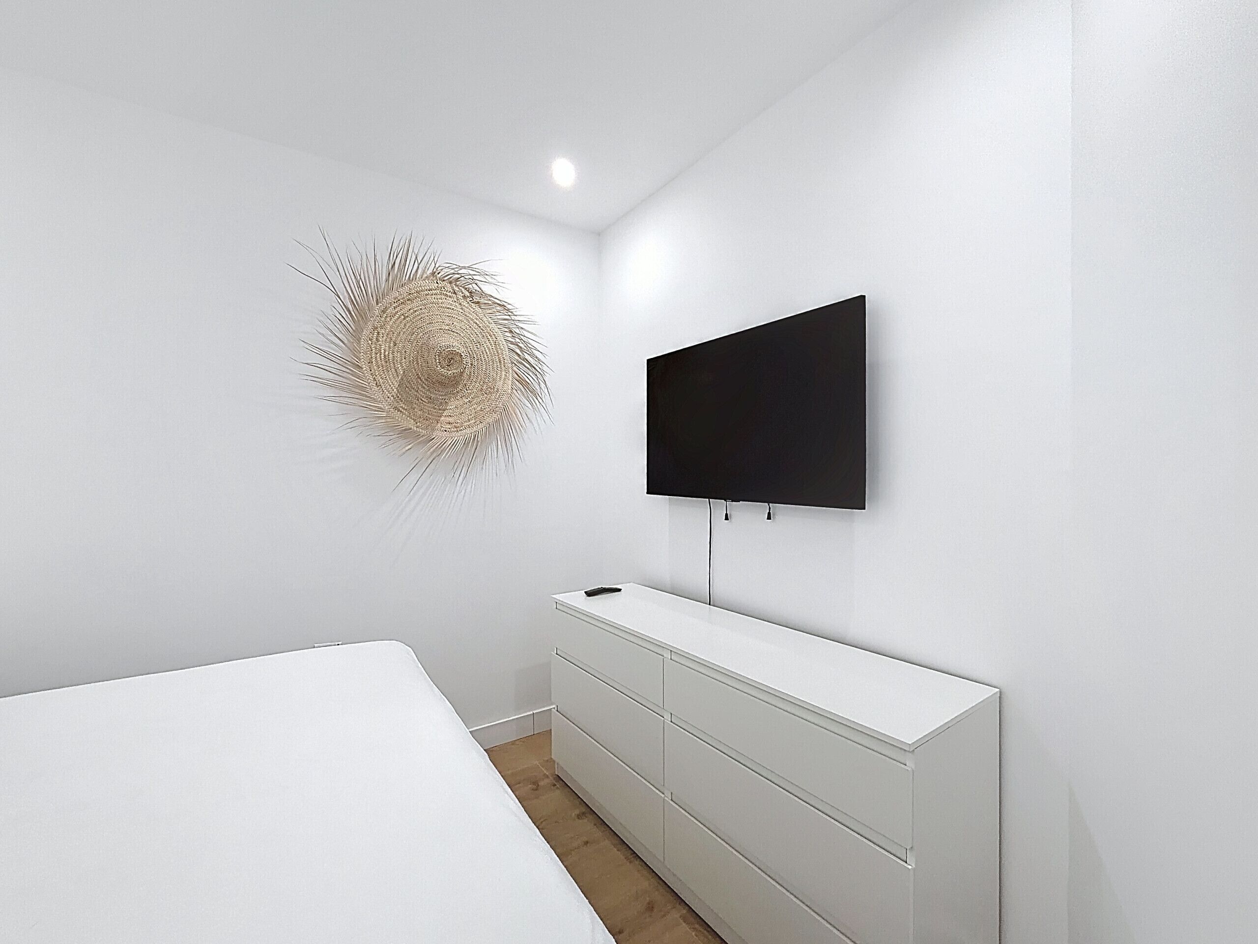 A modern room with a white bed, a white dresser, and a mounted TV.