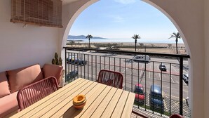 Un balcon avec vue sur la plage, une table avec un saladier et un canapé.