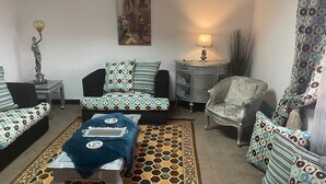 A living room with patterned sofas, a small table, a decorative lamp, and a painting on the wall. - One Bedroom Apartment City Views Local to Airport (Cairo)