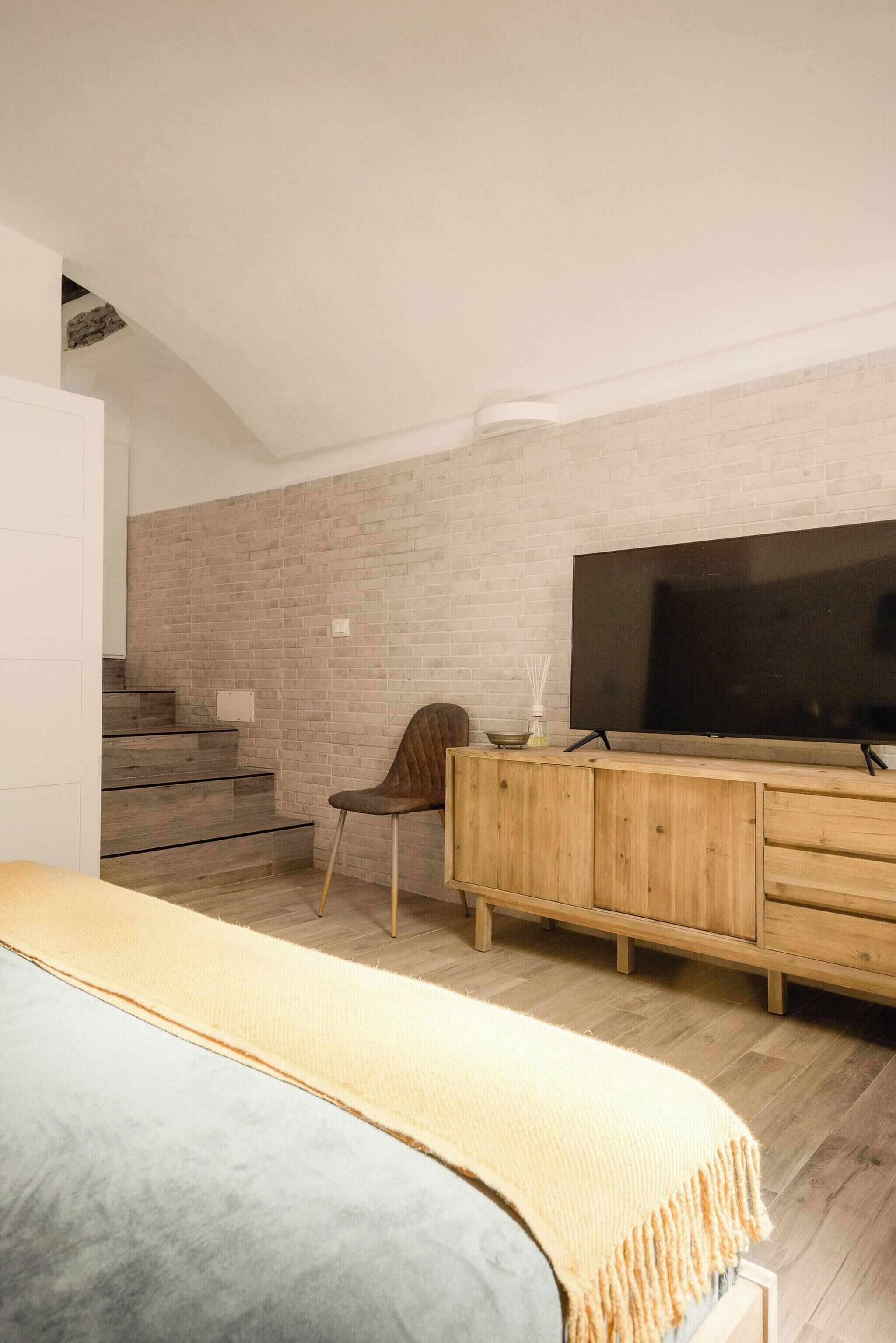 Une chambre moderne avec un grand lit, une commode en bois, une télévision et un escalier.