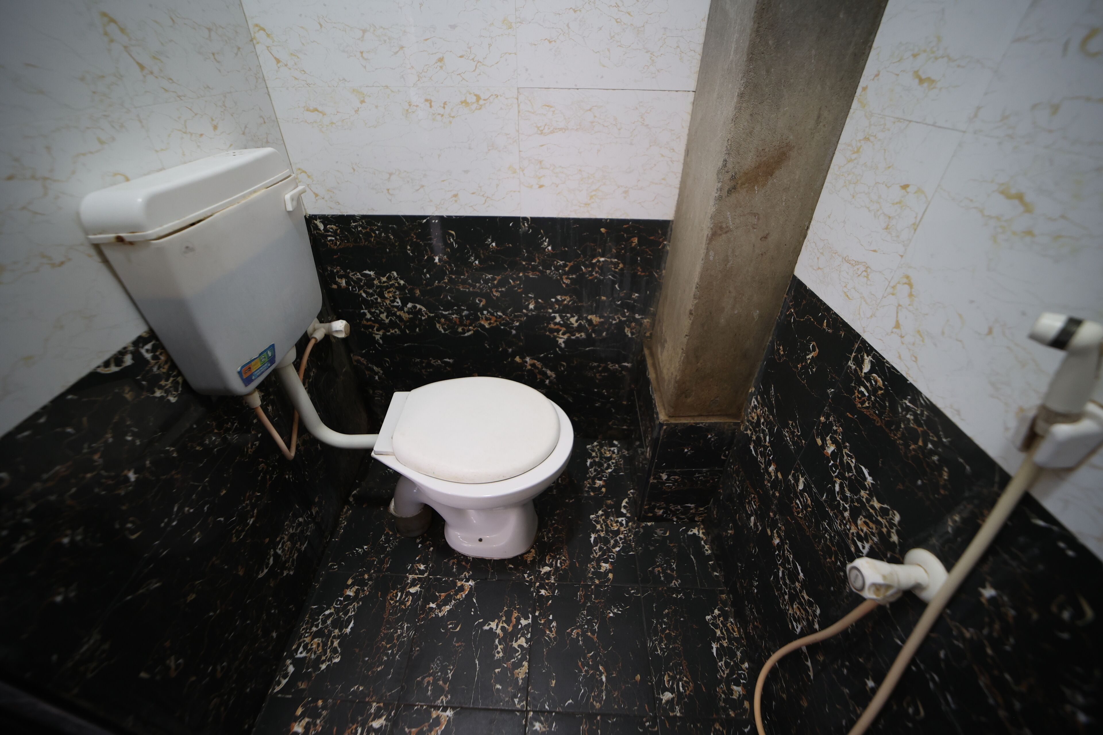 Ein Badezimmer mit Toilette, schwarzem Marmorboden und weißen Wänden mit Flecken.