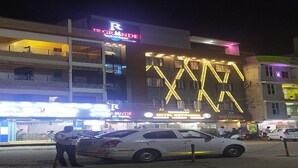 A hotel with a prominent 'GRANDE' sign, a large illuminated 'X' on the facade, and a white car parked in front. - JR Grande (Kilvelur)