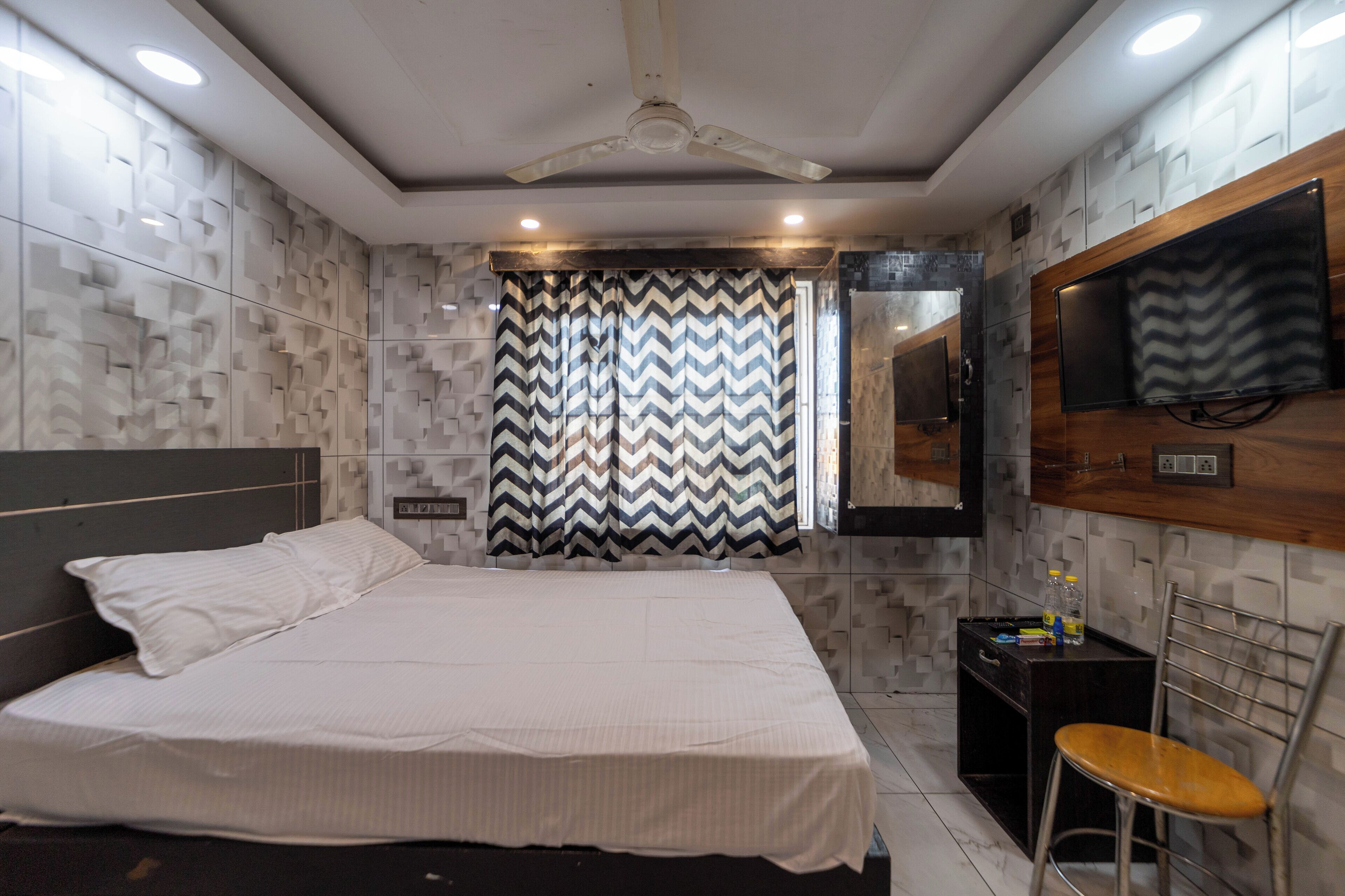 Una camera da letto moderna con un letto, una TV a muro, una ventola a soffitto e un tavolino con una sedia.