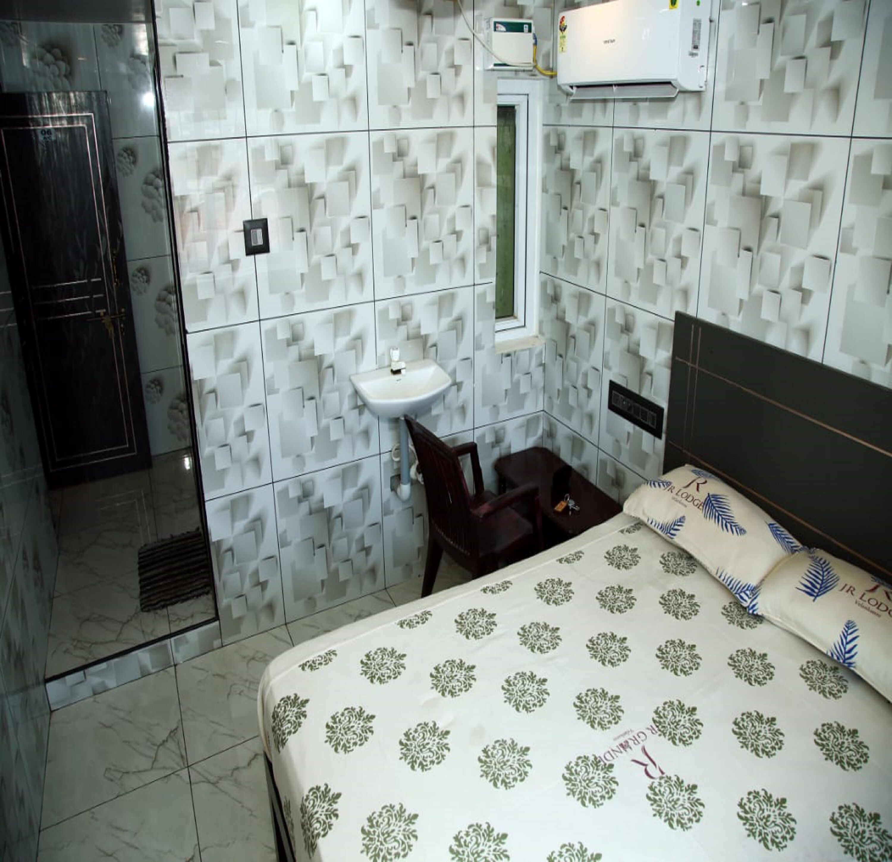 A hotel room with a bed, a bedside table, a chair, a sink, and a shower area.