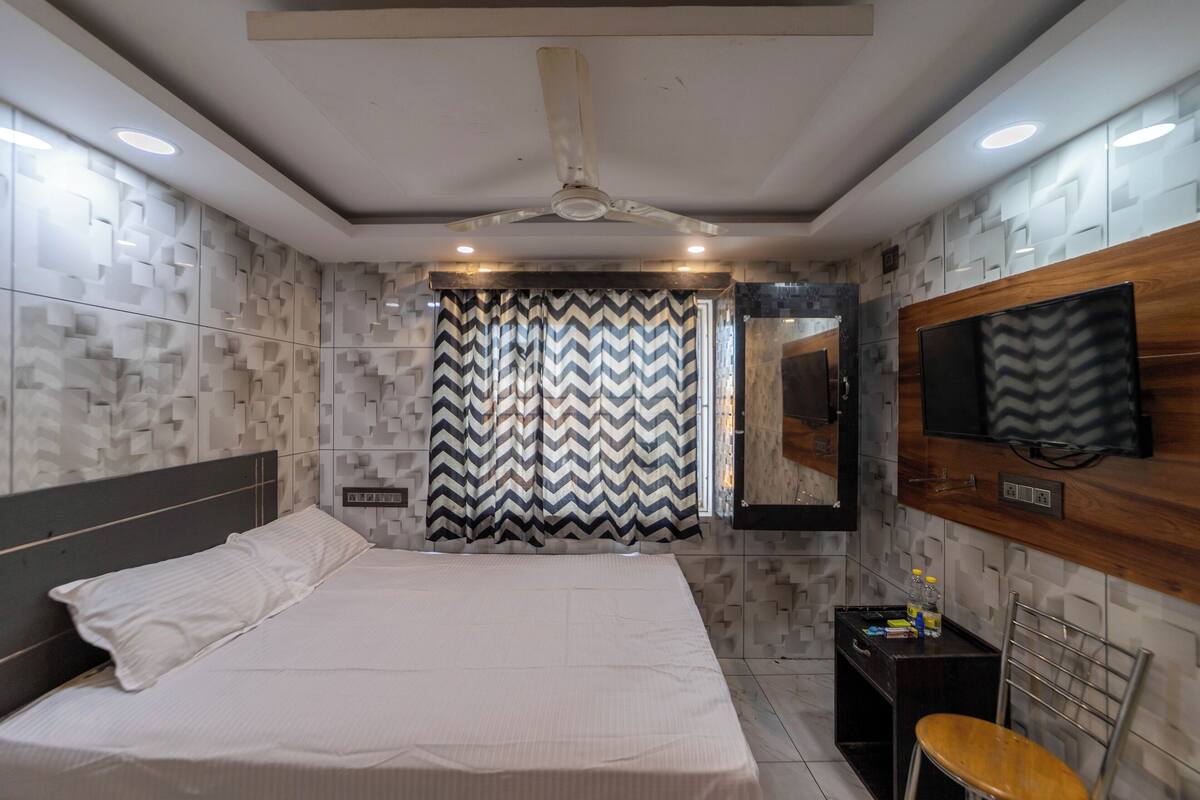 A modern bedroom with a large bed, a ceiling fan, a TV mounted on the wall, and a small table with a chair.