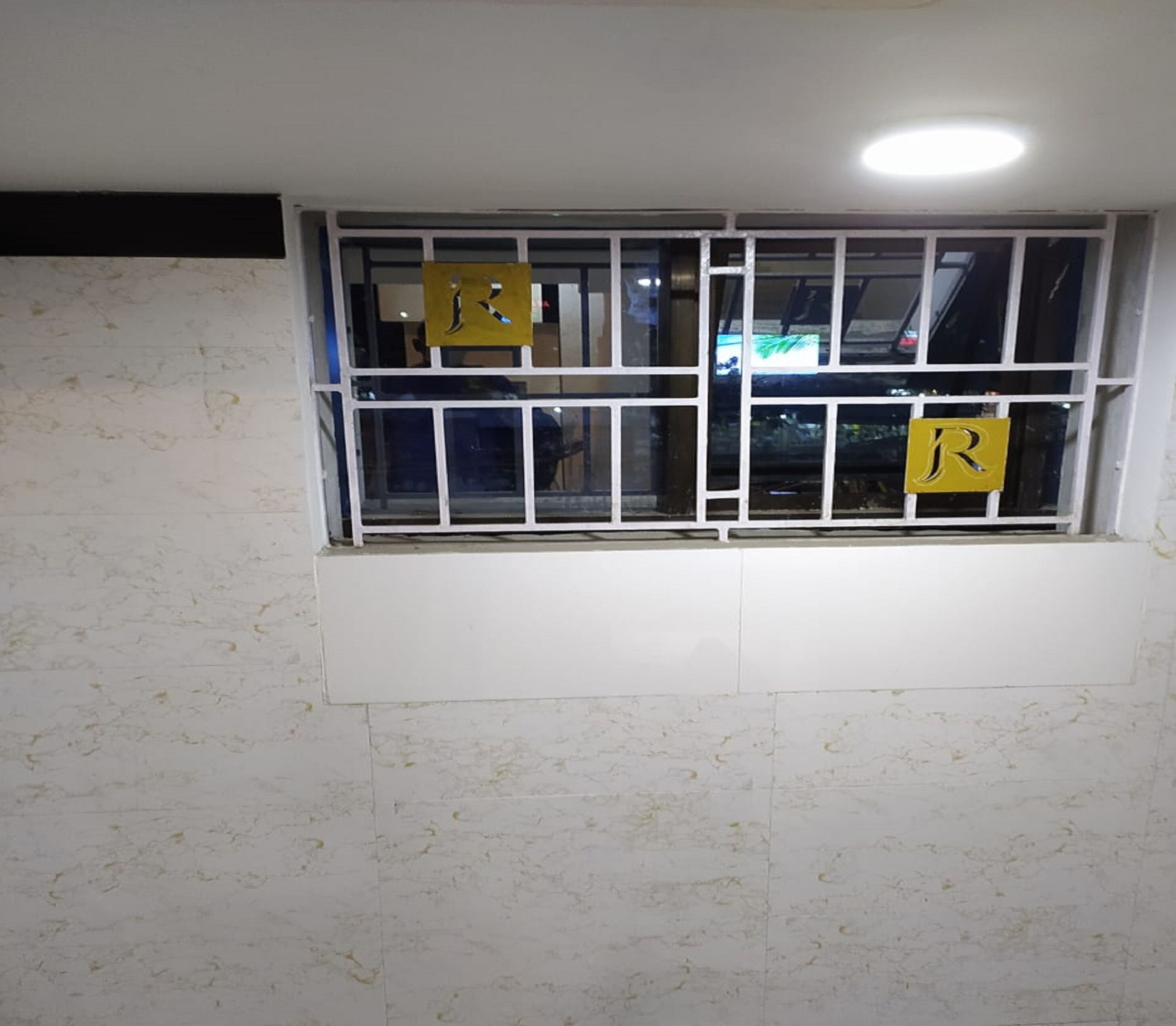 A window with a metal grid and two yellow signs with the letter 'R'.