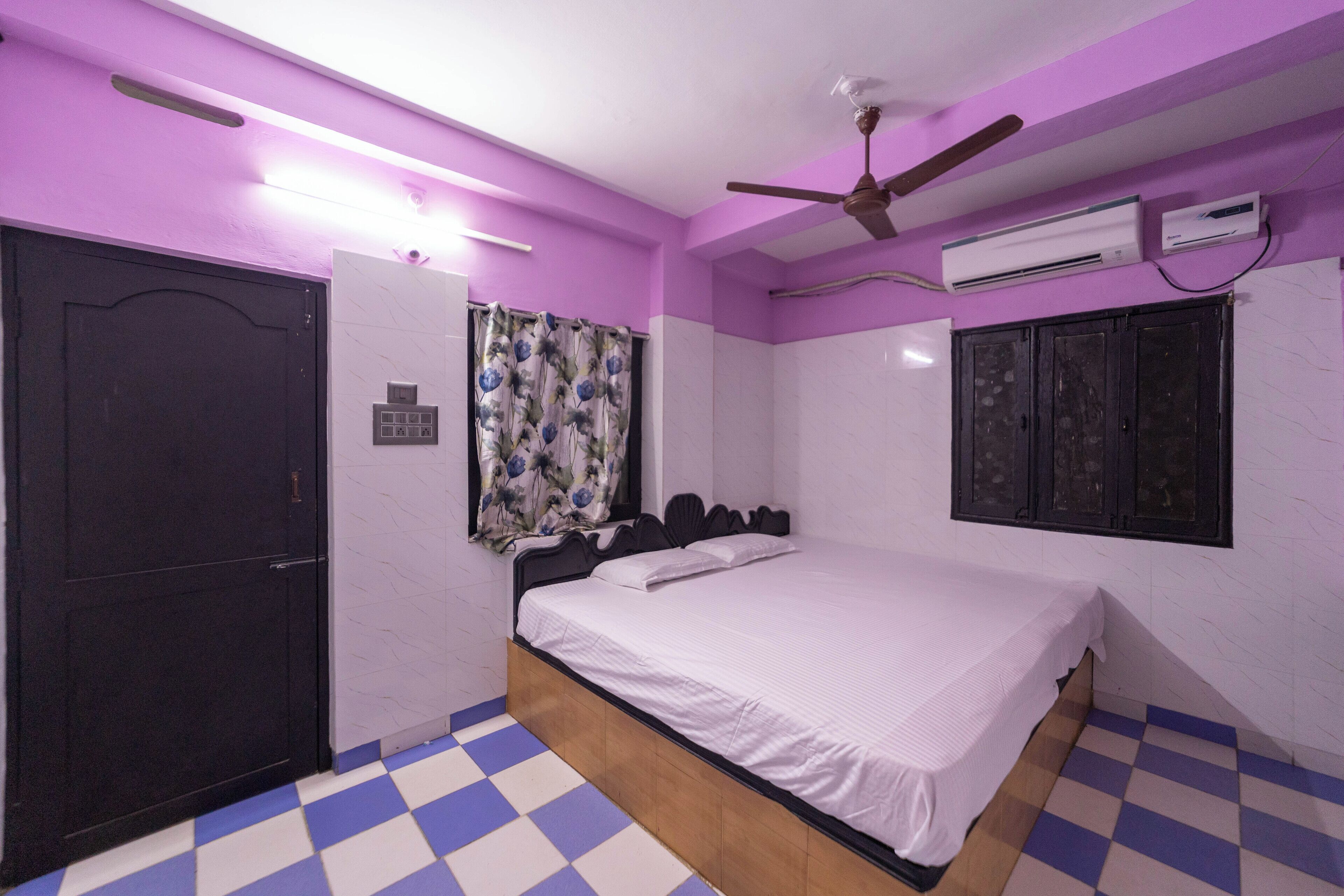 Un dormitorio con una cama, ventilador de techo, equipo de aire acondicionado, una puerta y piso a cuadros.
