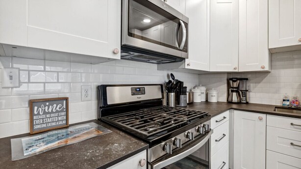Una cocina moderna con armarios blancos, estufa de acero inoxidable, microondas y cafetera.