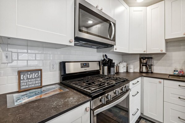A modern kitchen with white cabinets, a stainless steel stove, a microwave, and a coffee maker. - Beach Vibes on Lake Michigan (South Haven)