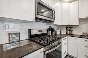 A modern kitchen with white cabinets, a stainless steel stove, a microwave, and a coffee maker.