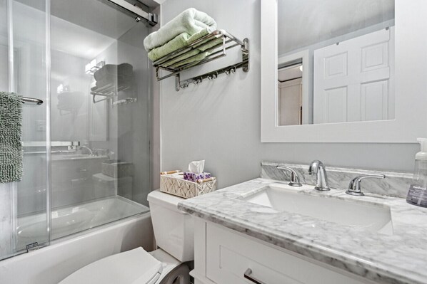 A modern bathroom with a glass shower enclosure, a marble sink, and a towel rack with folded towels.