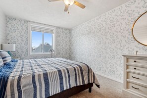 Une chambre à coucher avec un lit, une fenêtre, un ventilateur de plafond et une commode.