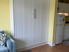 A room with a large wardrobe, a sofa with a patterned cushion, and a kitchen area with a refrigerator. - Beach and pool are right there to enjoy! (South Haven)