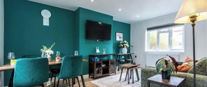 A teal-colored room with a TV, dining table, chairs, and a sofa. - 3BR House in Beeston Ideal for Corporate Stays (Beeston)