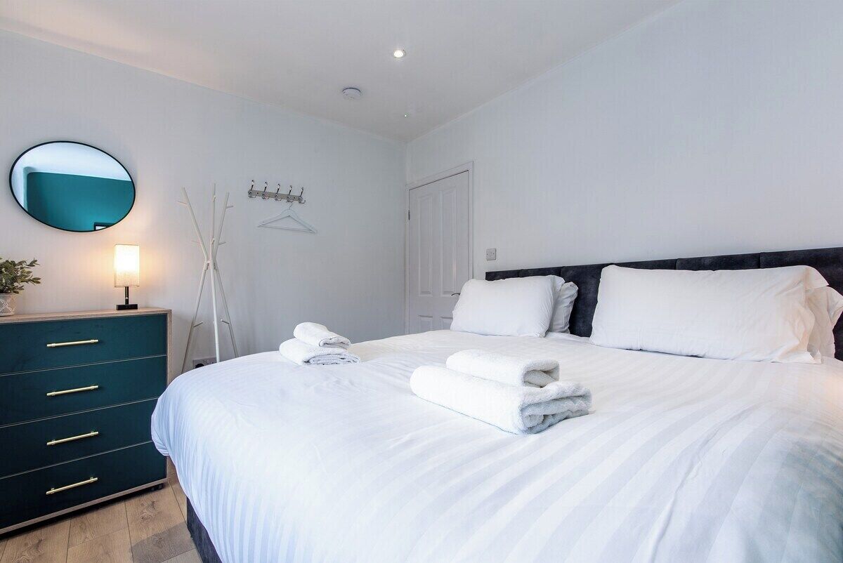 A bedroom with a bed, bedside tables, a mirror, and a wall-mounted light fixture.