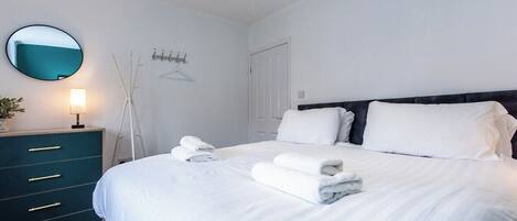A bedroom with a bed, bedside tables, a mirror, and a wall-mounted light fixture.
