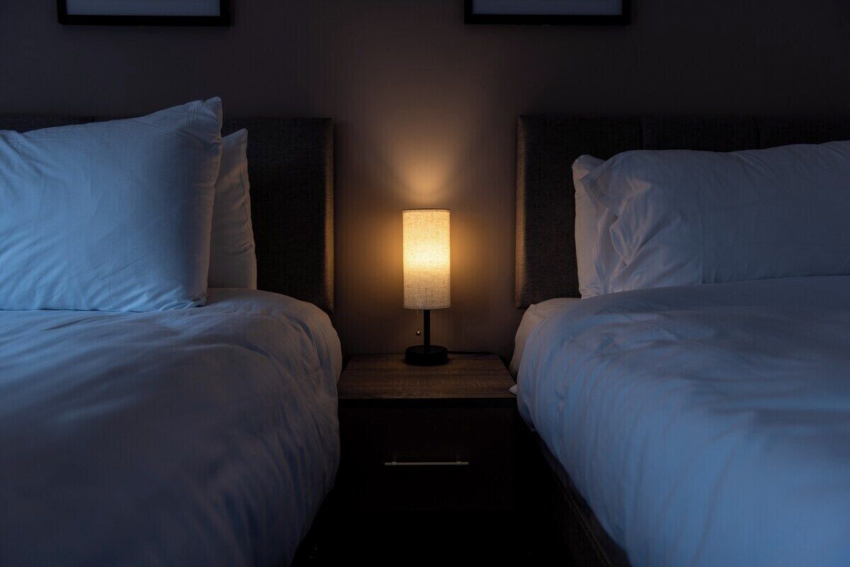 A hotel room with two beds, a nightstand with a lamp, and framed pictures on the wall.