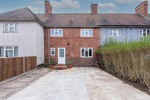 A two-story residential building with a front door, two windows on the ground floor, and a small front yard with a wooden fence and potted plants. - 3BR House in Beeston Ideal for Corporate Stays (Beeston)
