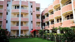 Un edificio residencial de varios pisos con balcones, un pequeño jardín y una estructura de techo rojo.