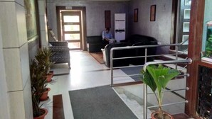Zona de recepción con mostrador, sillas, plantas en macetas y una puerta que da a otra habitación.