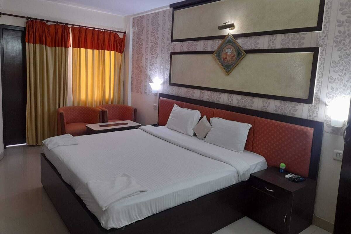 A hotel room with a large bed, a small table, a chair, and a nightstand with a lamp.