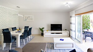 Un salon moderne comprenant un coin repas, un téléviseur à écran plat et une porte-fenêtre coulissante donnant sur un espace extérieur.