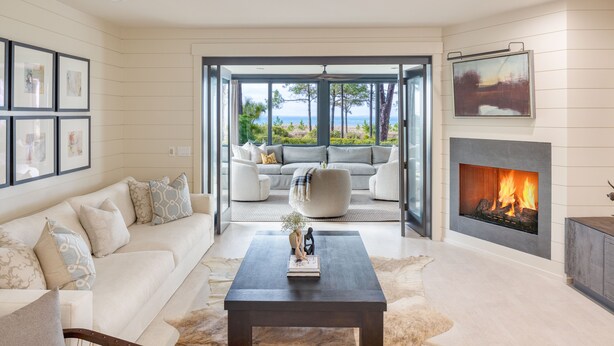 A modern living room with a sofa, coffee table, fireplace, and a view of the outdoors. - South Beach Serenity by AvantStay | Private Pool + Beachfront (Hilton Head Island)