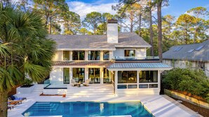 A modern house with a large pool, a covered patio, and a view of tall trees. - South Beach Serenity by AvantStay | Private Pool + Beachfront (Hilton Head Island)