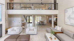 A spacious living area with a high ceiling, a balcony with a railing, and a dining area in the background. - South Beach Serenity by AvantStay | Private Pool + Beachfront (Hilton Head Island)