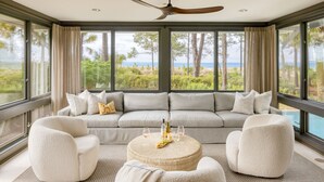 A modern living room with a large gray sectional sofa, two white armchairs, and a round coffee table with wine bottles and glasses. - South Beach Serenity by AvantStay | Private Pool + Beachfront (Hilton Head Island)