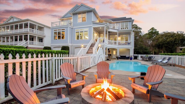 A two-story house with a pool, outdoor seating, and a fire pit.