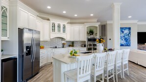 A modern kitchen with white cabinetry, a stainless steel refrigerator, and a central island with bar stools.