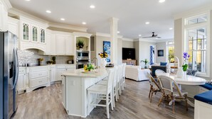 A spacious kitchen with white cabinetry, a central island, and a dining area with wicker chairs.