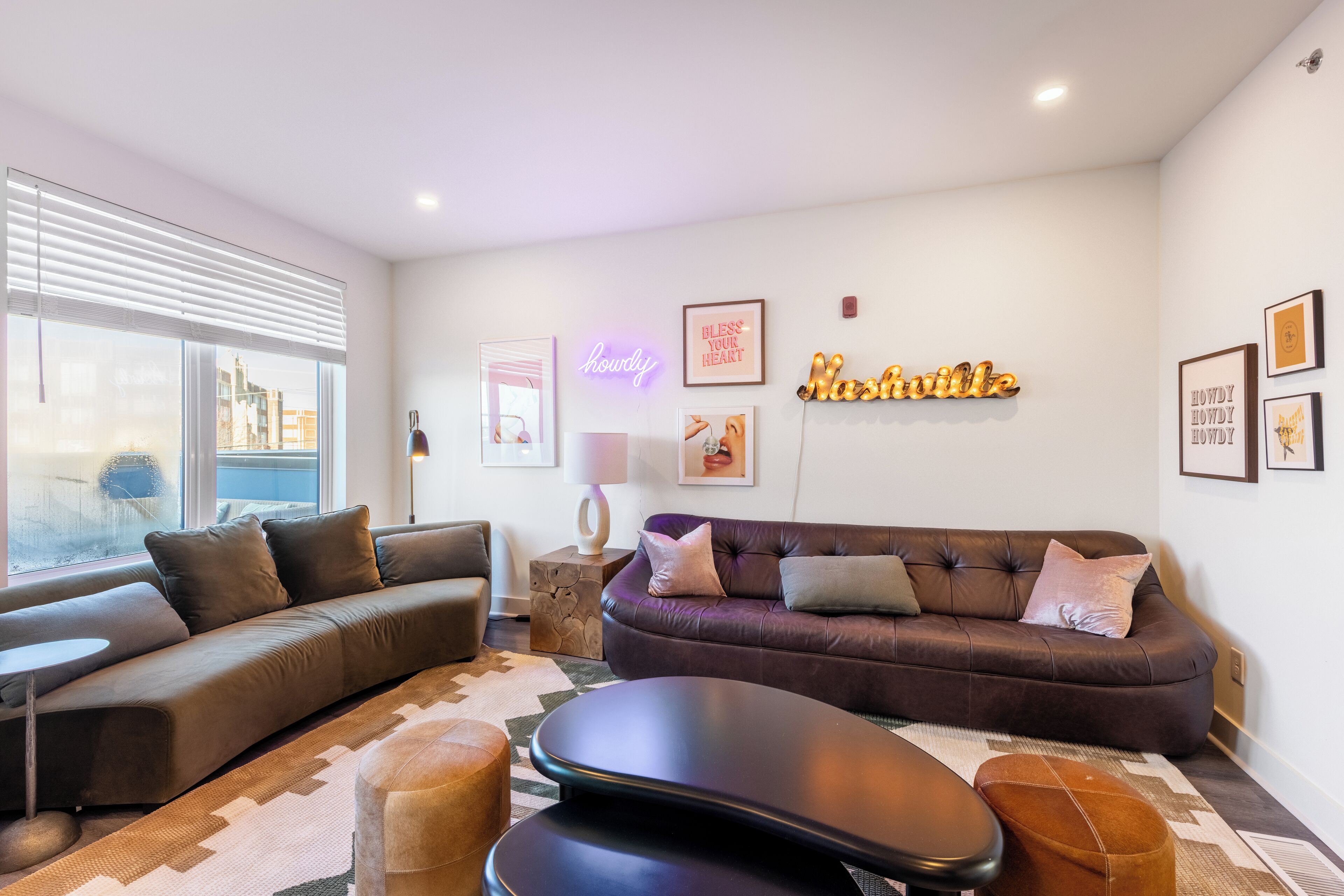 A modern living room with a dark brown leather sofa, a black ottoman, and a patterned rug.