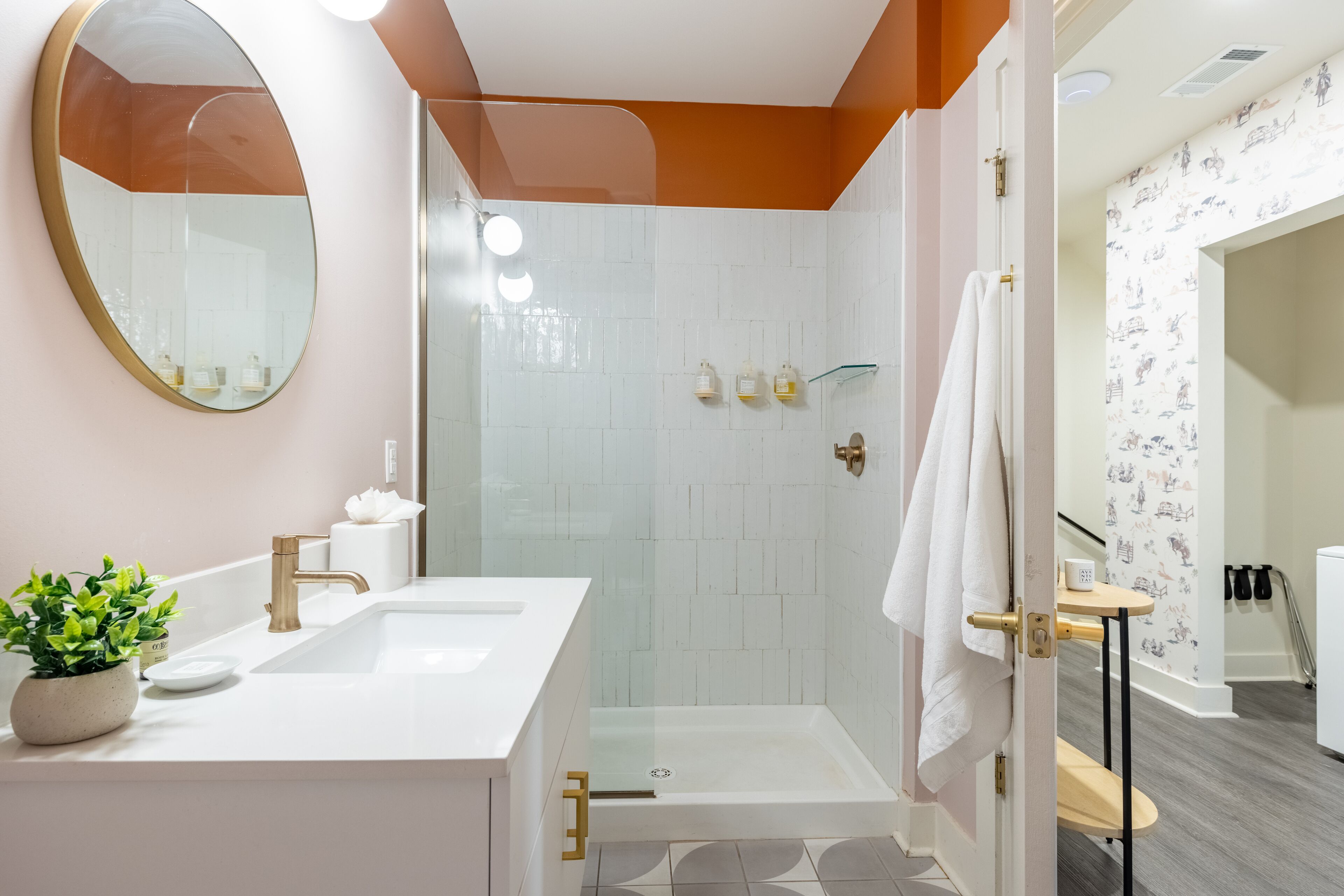 A modern bathroom with a large mirror, a sink, a shower, and a small table with a towel.