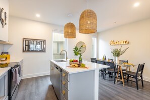 Een moderne keuken met een centraal eiland, hanglampen, en een eethoek met een tafel en stoelen.