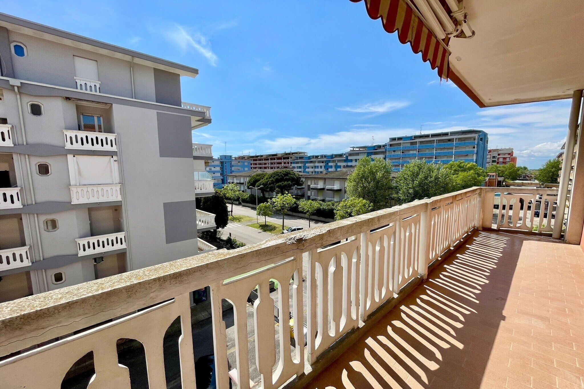 Ein Balkon mit weißer Brüstung mit Blick auf ein Wohngebiet mit mehrstöckigen Gebäuden.