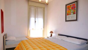 A room with two beds, a window with curtains, a wall-mounted lamp, and a framed artwork. - Apartment in Caorle near Sandy Beaches (Caorle (VE))