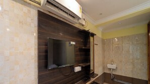 Un baño moderno con televisor de pantalla plana sobre un mueble de tocador de madera oscura, zona de ducha y un inodoro.