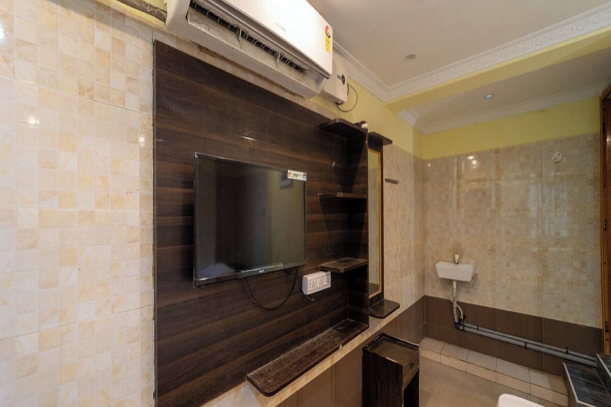 A modern bathroom with a flat-screen TV mounted on a dark wood vanity, a shower area, and a toilet.